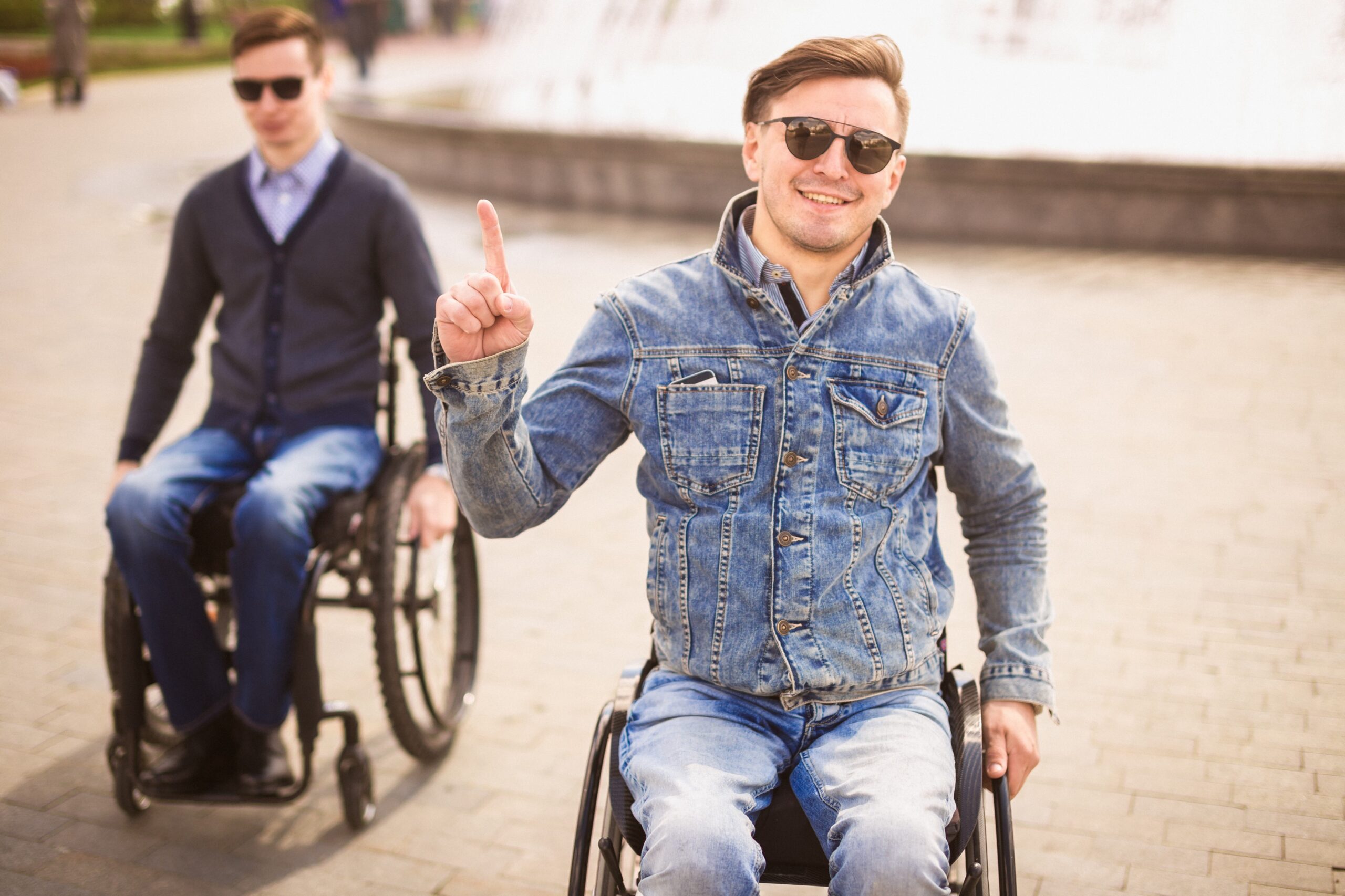 Foto van twee mannen, beide zittend in een rolstoel. Een man steekt zijn duim op.