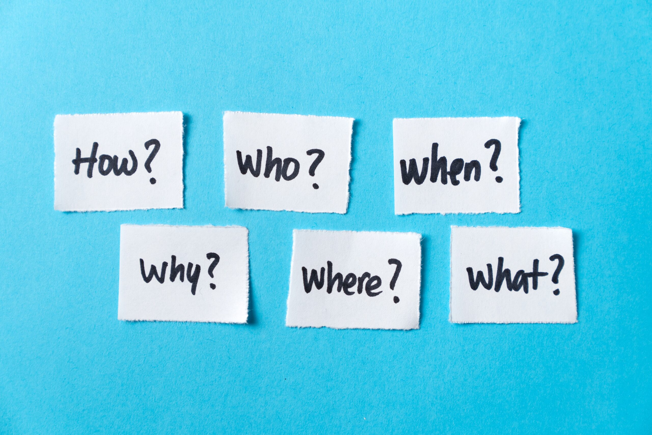 Een blauw vlak met witte memobriefje met de woorden, how, who, when, why., where, what beschreven